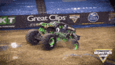 a monster jam truck is on a dirt track in front of a great clips sign