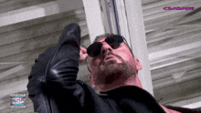 a man wearing sunglasses and a leather jacket is looking up at something