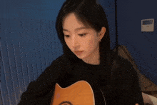 a woman is playing an acoustic guitar in a dark room