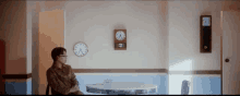 a man is sitting at a table with a clock on the wall above him