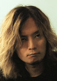 a man with long blonde hair looks at the camera with a serious look on his face