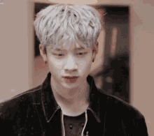 a young man with white hair and earrings is wearing a black jacket .