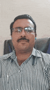 a man wearing glasses and a striped shirt is sitting in a chair and looking at the camera