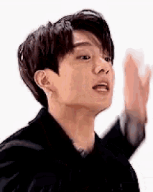 a young man in a black suit is waving his hand .