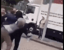 a group of people are standing in front of a white truck on the side of the road .