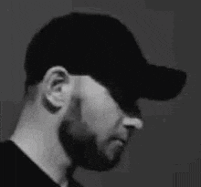 a black and white photo of a man wearing a baseball cap and a beard .