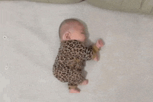 a baby wearing a leopard print outfit is sleeping on a bed .