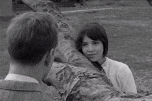 a man and a woman are standing next to a tree trunk .