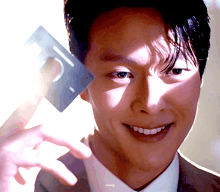 a man in a suit is smiling and holding a credit card in his right hand