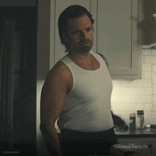 a man in a white tank top stands in a kitchen with thunderbolts written on the corner
