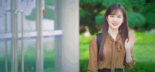 a woman in a brown blouse is smiling and waving at the camera