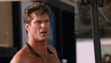 a shirtless man with headphones around his neck looks at the camera with his mouth open