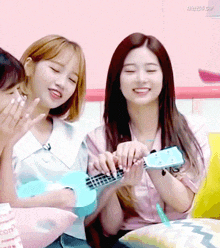 a girl is playing an ukulele while another girl looks on