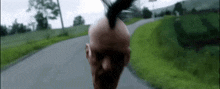 a bald man with a mohawk is walking down the road .
