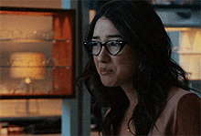 a woman wearing glasses is standing in front of a glass display case .