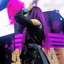 a woman with purple hair is standing on a stage holding her hair .