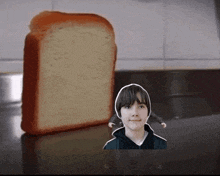 a boy is standing next to a loaf of bread on a counter