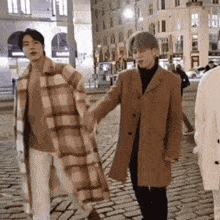 a couple of men are holding hands while walking down a cobblestone street .