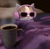 a cat wearing pink headphones and sunglasses is sitting next to a cup of coffee .