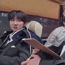 a young man is sitting on a bus holding a clipboard and a pen .