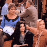 three women are sitting on a couch with a man sitting at a table in the background