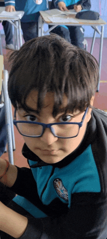 a young boy wearing glasses and a blue and black jacket with a badge on the sleeve