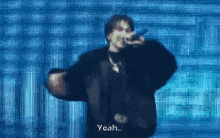 a man in a black jacket is singing into a microphone and the word yeah is visible