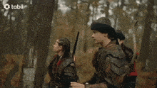 a man in armor is talking to a woman with a tabli logo on the bottom