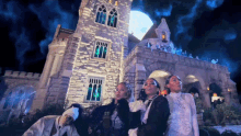 a group of people standing in front of a castle with a full moon in the background