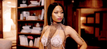 a woman in a bra and earrings is standing in front of a bookshelf in a living room .