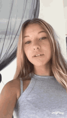 a young woman in a grey tank top is taking a selfie with her phone .