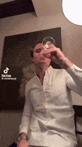 a man in a white shirt is drinking from a wine glass with a tiktok watermark