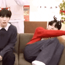 two men are sitting on a couch with one wearing a reindeer headband and the other wearing a red sweater .