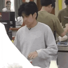 a man in a grey sweater is standing in front of a counter .