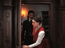 a woman in a red dress stands in front of a man in a black suit