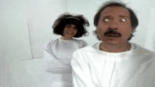 a man with a mustache and a woman in a straight jacket are standing next to each other .