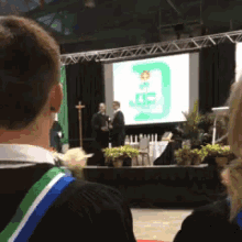 a group of people are sitting in front of a stage with a screen that says ' oe ' on it