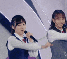 a girl singing into a microphone while another girl looks on