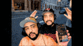 two men wearing headphones and hats are holding up their phones