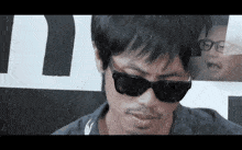 a man wearing sunglasses is standing in front of a sign that says t