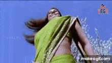 a woman in a green saree is standing in front of a tree .