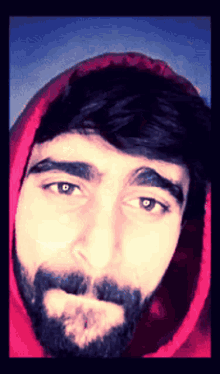 a man with a beard and a red hoodie looks at the camera