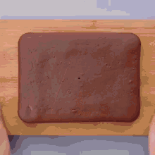 a person is cutting a piece of chocolate cake on a wooden cutting board .