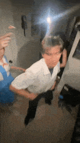 a man in a white shirt is dancing in a room with a woman in a blue dress behind him .