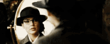 a woman in a hat and glasses is looking at herself in the mirror .