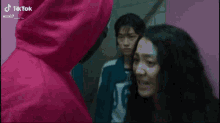 a man in a red hoodie is standing next to a woman in a pink room .