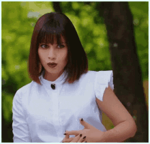 a woman with short hair and bangs is wearing a white shirt and black nail polish .