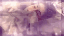a woman is laying on a bed with her eyes closed and a purple background .