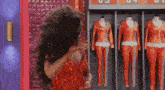 a drag queen in a red dress is standing in front of a row of mannequins .