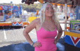 a blonde woman in a pink tank top stands in front of a carnival booth